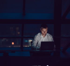 A man working at a computer in an office, late at night.