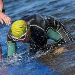 A swimmer in a wetsuit crawling out of a lake