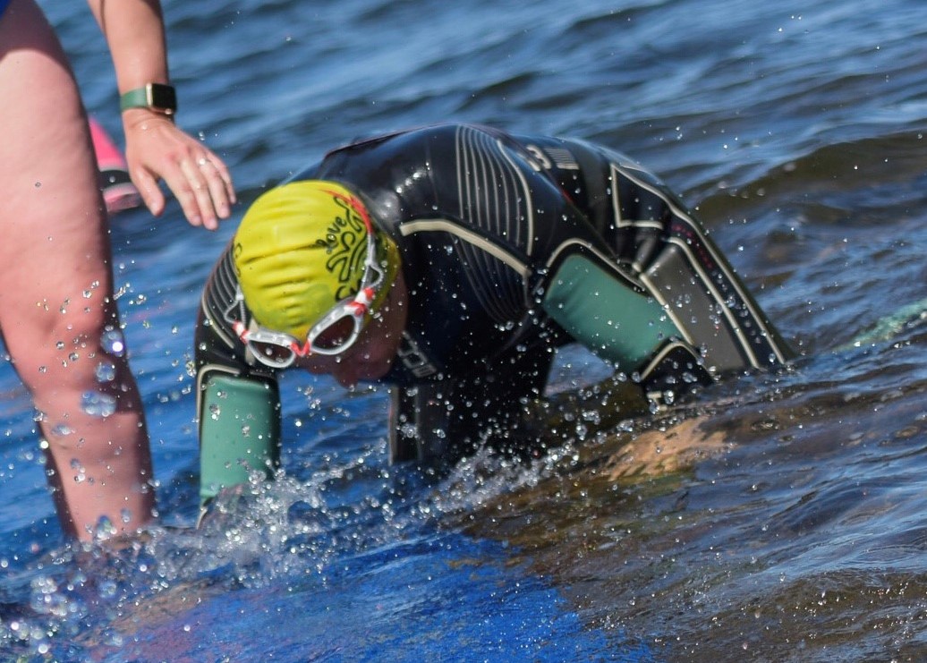 A swimmer in a wetsuit crawling out of a lake