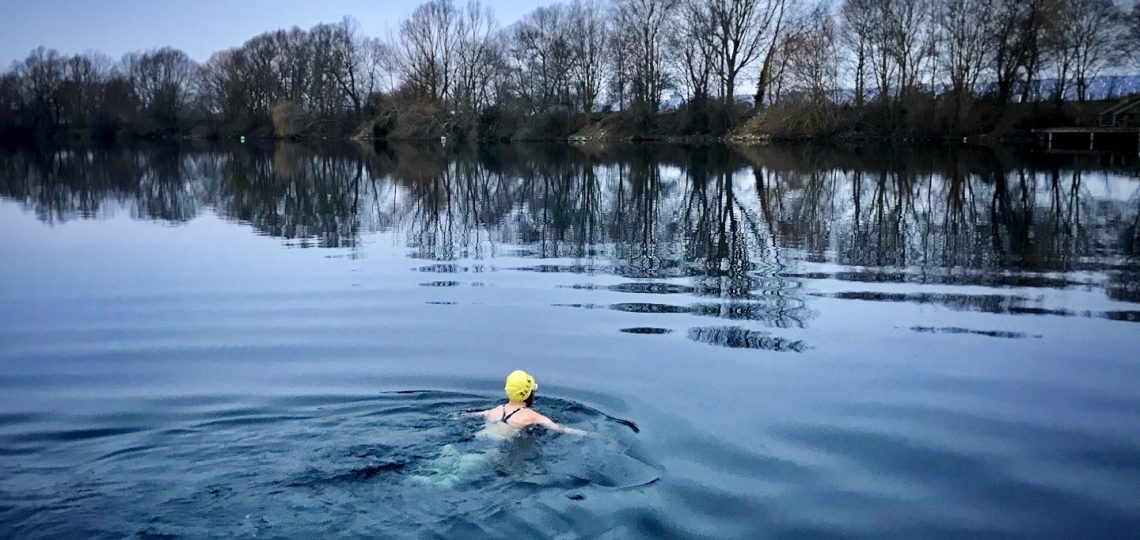 A swimming in a lake in winter doing breaststroke away from the camera