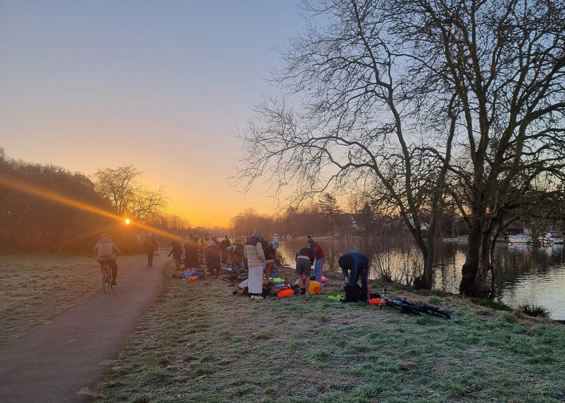 A group of swimmers changing by a river at sunrise. Frost on the ground.
