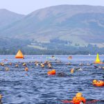 Lots of swimmers in Loch Lomond swimming away from the camera towards the hills in the background