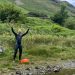 Matt Dawson celebrating with raised arms after finishing his final Lake District swim. Green hills in the background.