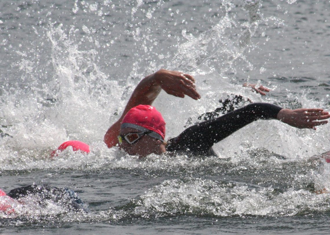 Close up of two swimmers in open water. The one nearest the camera has their head up looking forward.