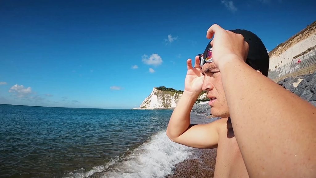 Andy Donaldson side profile shot adjusting his goggles while standing on a beach with white cliffs behind him.