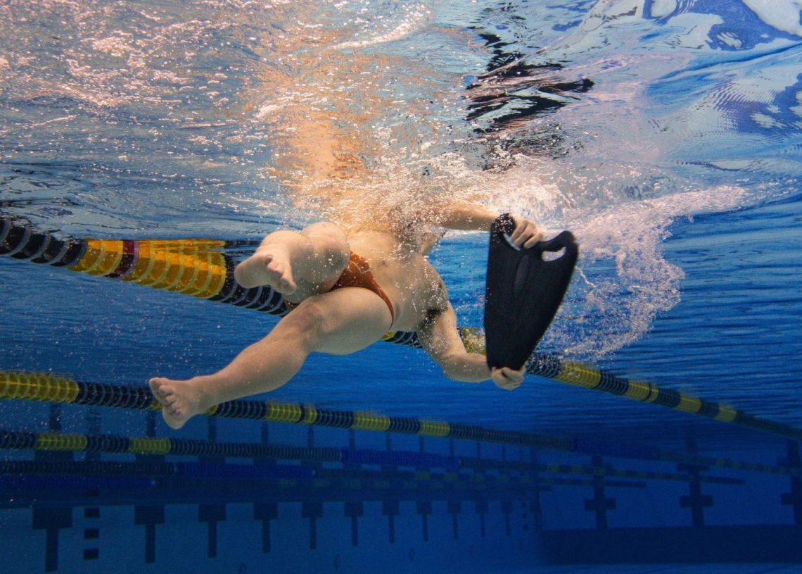Underwater view of a swimmer swimming away from the camera on their back while holding a float.