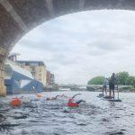 A group of swimmers and paddle boarders going under a bridge