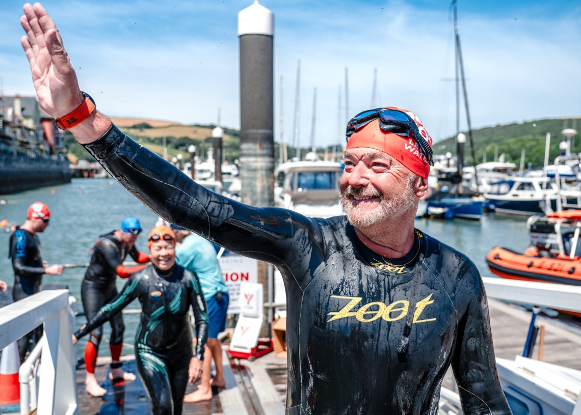 A swimmer in a wetsuit proudly waving at the end of the Dart10k