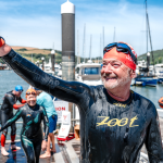 A swimmer in a wetsuit proudly waving at the end of the Dart10k